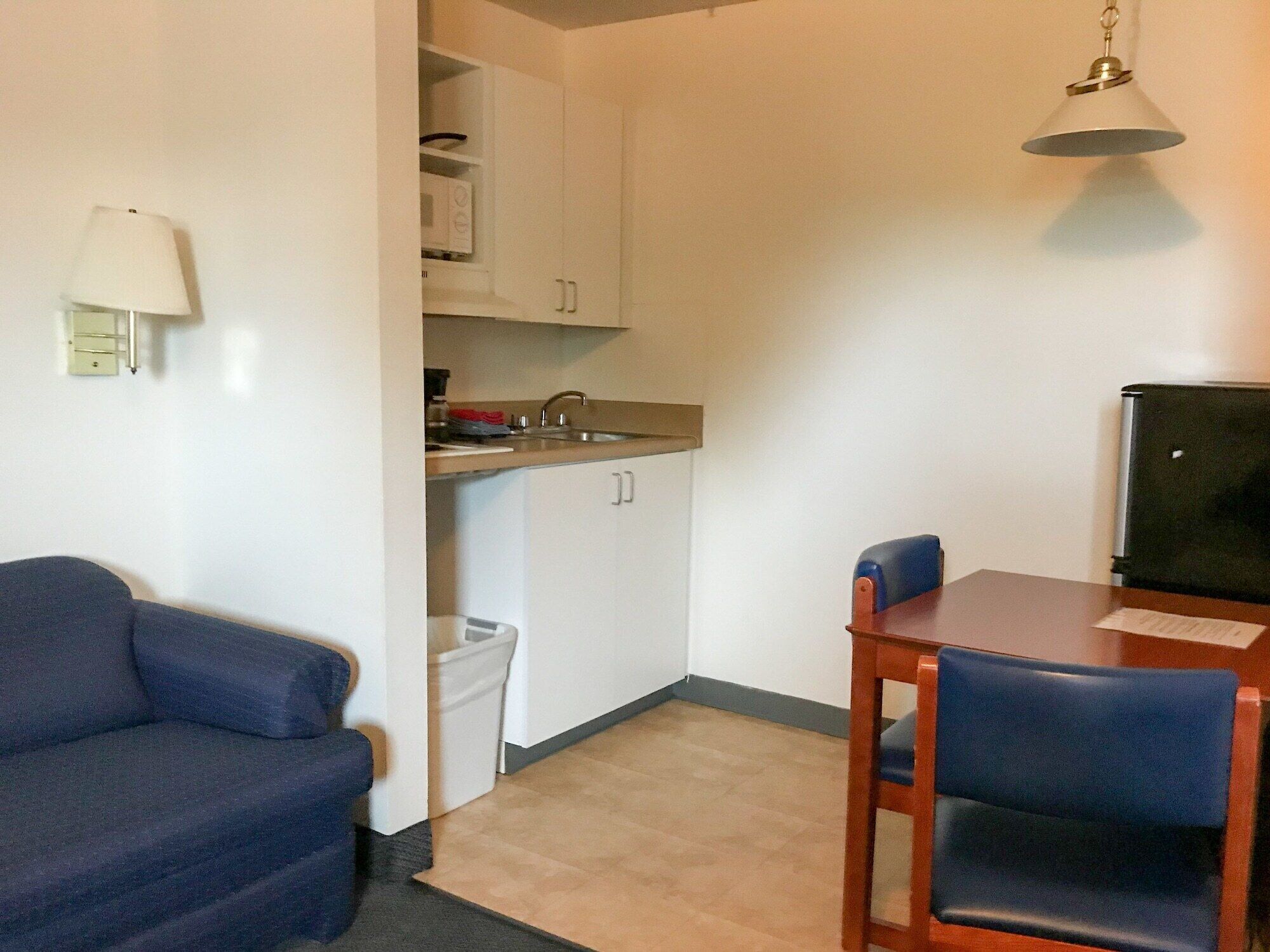 A compact living space with a kitchenette, a dining table with chairs, a sofa, and a lamp.