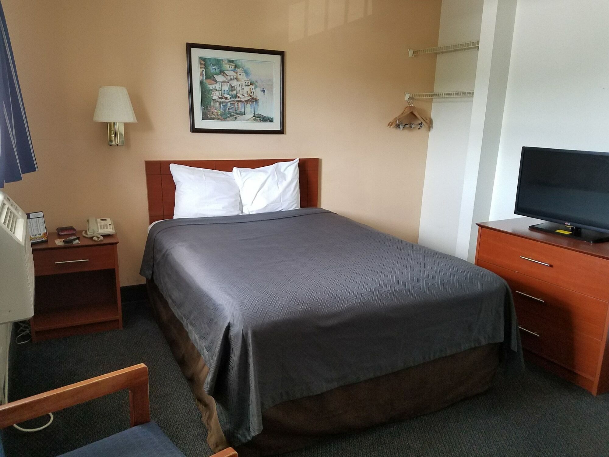 Une chambre d’hôtel avec un lit, un bureau avec un téléphone, une télévision et un tableau encadré au mur.