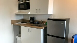 Una cuina compacta amb armaris blancs, un frigorífic d'acer inoxidable, un microones, una cafetera i un rentapeus.