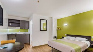 Habitación de hotel pequeña con cama, un escritorio, una silla, un espejo y una pared verde decorativa.