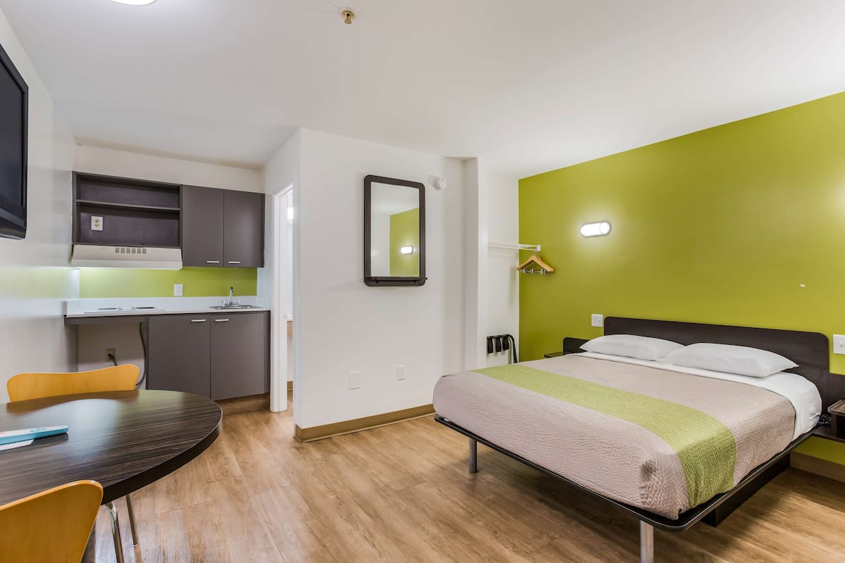 Habitación de hotel pequeña con cama, un escritorio, una silla, un espejo y una pared verde decorativa.