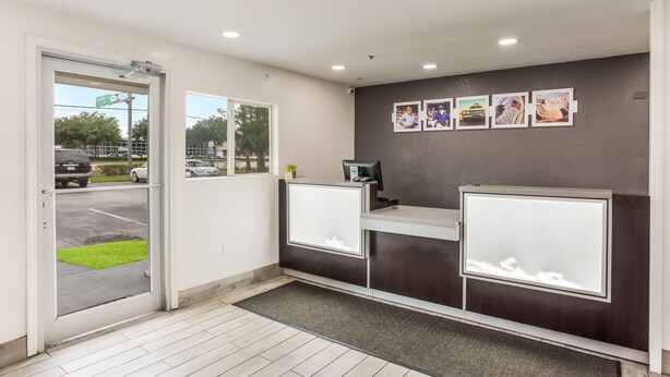Zona de recepción con puerta de vidrio, mostrador de recepción y pared con cuadros enmarcados.