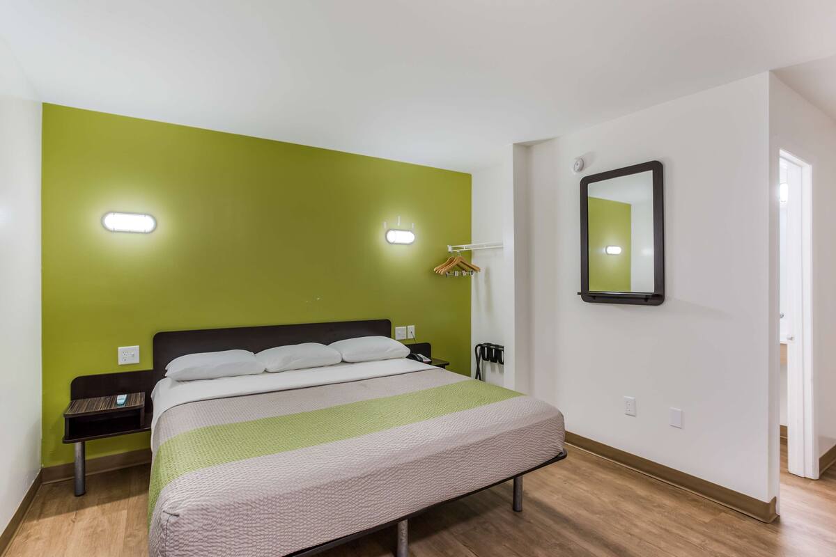 Una habitación de hotel con una cama, una mesita de noche, un espejo y una pared verde.