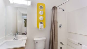 Une salle de bain moderne avec un lavabo, des toilettes et une douche, le tout de couleur blanche. On y trouve également un porte-serviettes jaune avec quatre serviettes.