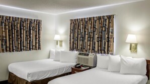 Ein Hotelzimmer mit zwei Betten, jeweils mit weißer Bettwäsche und einem braunen Betttuch. Zwischen den Betten befinden sich zwei Nachttische mit Lampen und ein Heizgerät. Die Vorhänge haben ein geometrisches Muster.