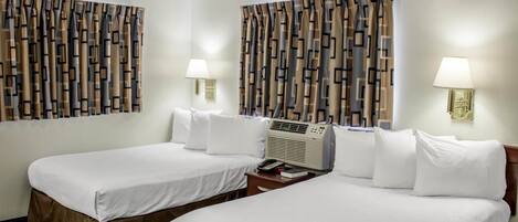 Une chambre d’hôtel avec deux lits, chacun recouvert de draps blancs et agrémenté d’une housse de lit marron. Il y a deux tables de chevet avec des lampes, et un radiateur est placé entre les deux lits. Les rideaux présentent un motif géométrique.
