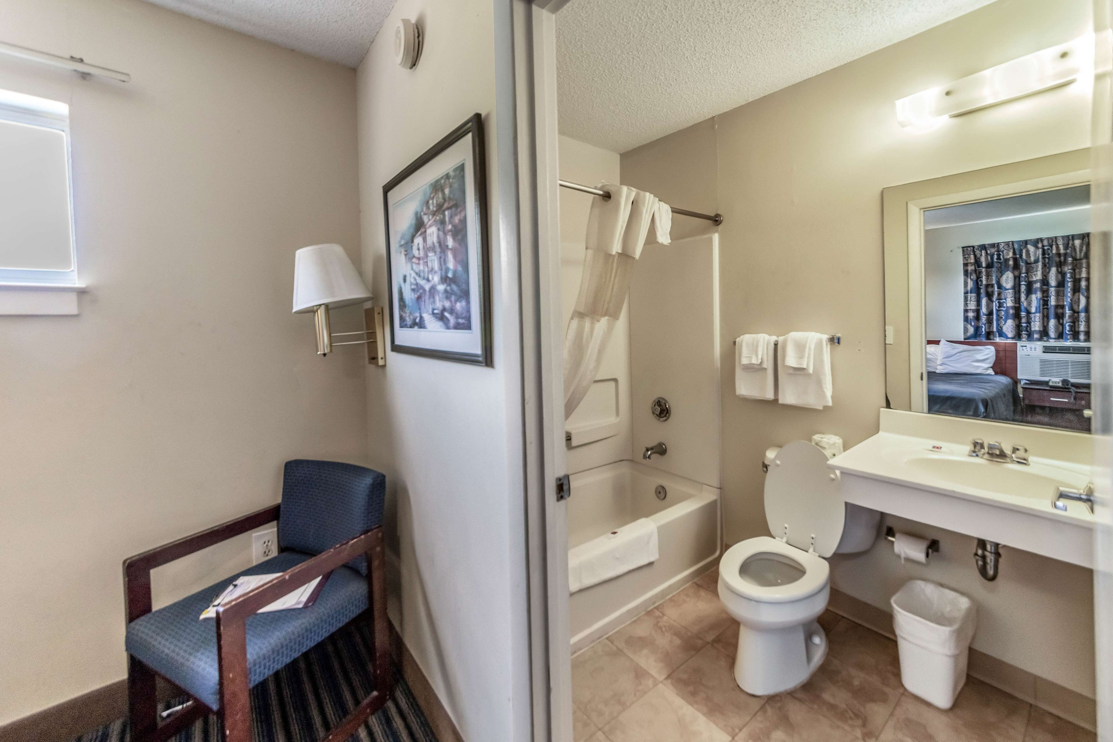 Un baño con bañera, inodoro, lavamanos y una silla.