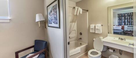 A bathroom with a bathtub, toilet, sink, and a chair.