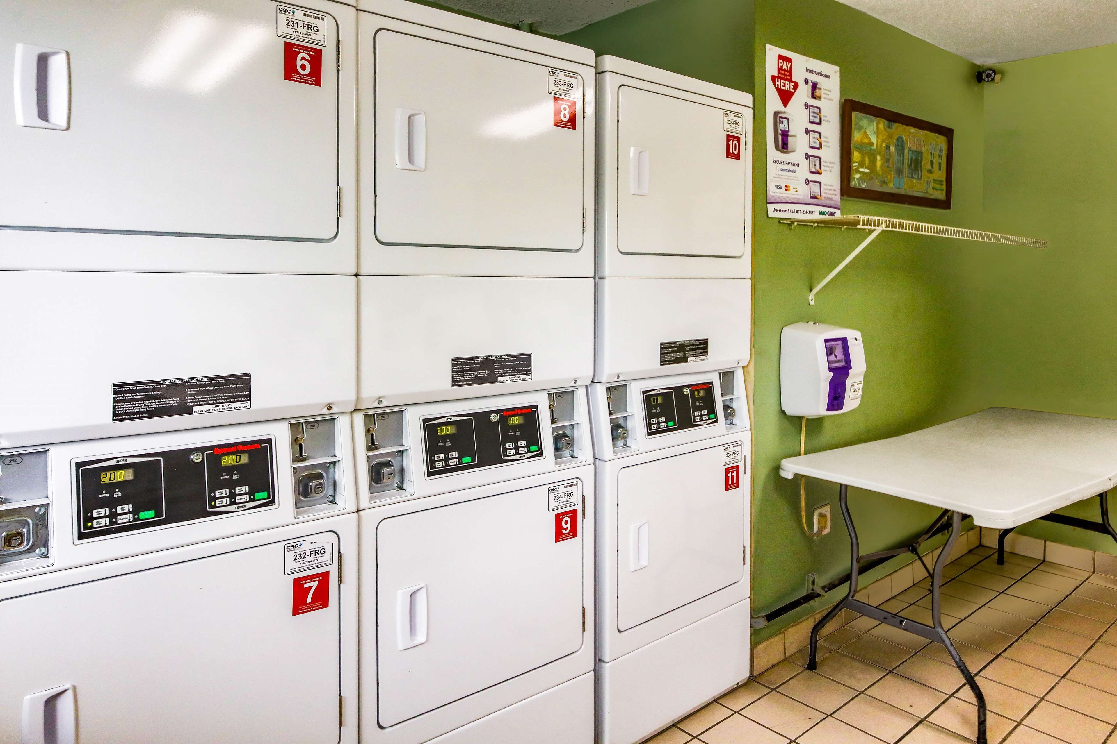 A laundry room with multiple white dryers, numbered from 6 to 11, and a table with a purple machine.