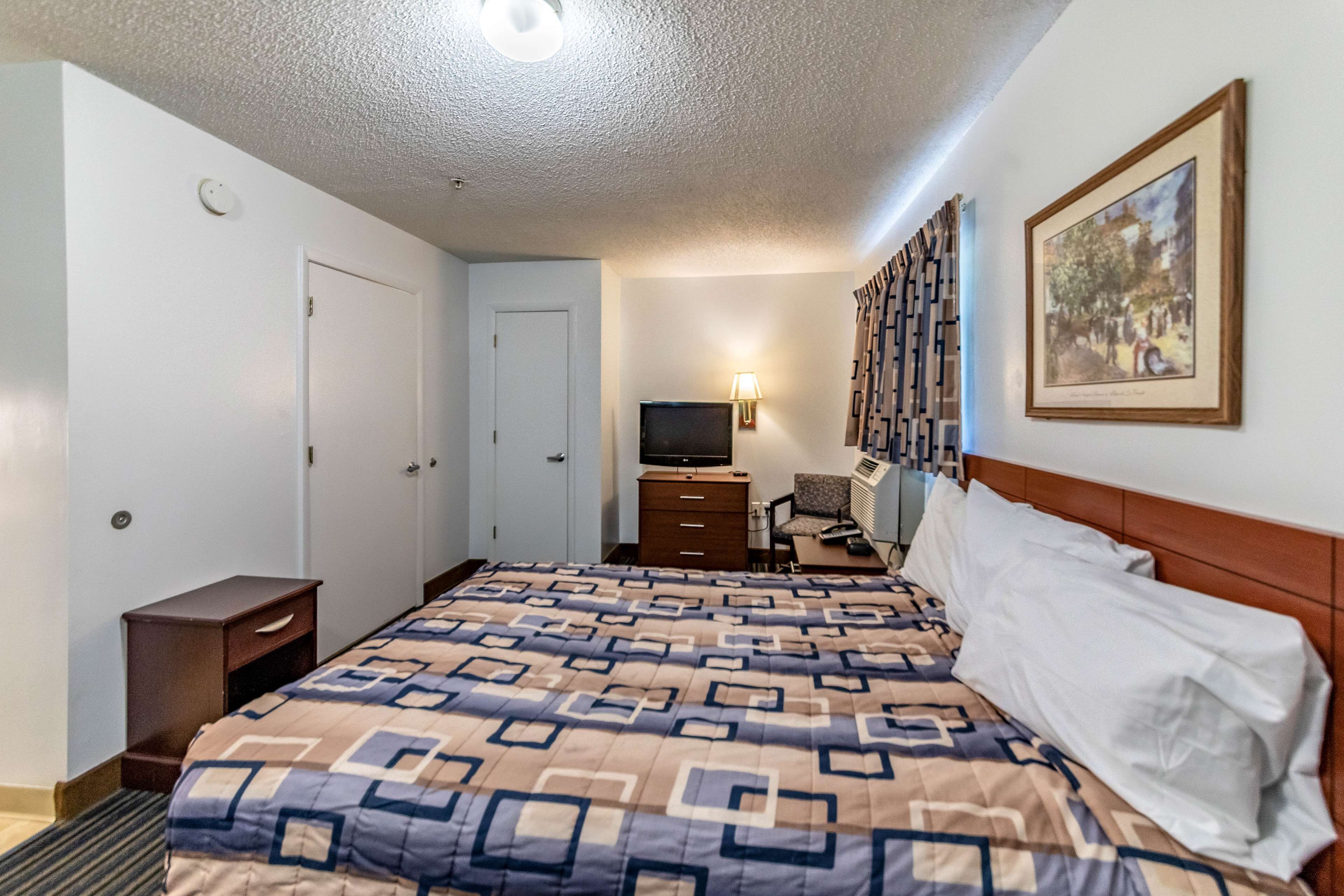 A hotel room with a large bed, a television, a desk, and a chair.