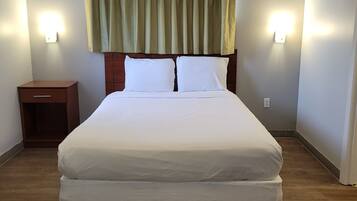 A hotel room with a large bed, wooden headboard, two bedside lamps, a nightstand, and a window with curtains.