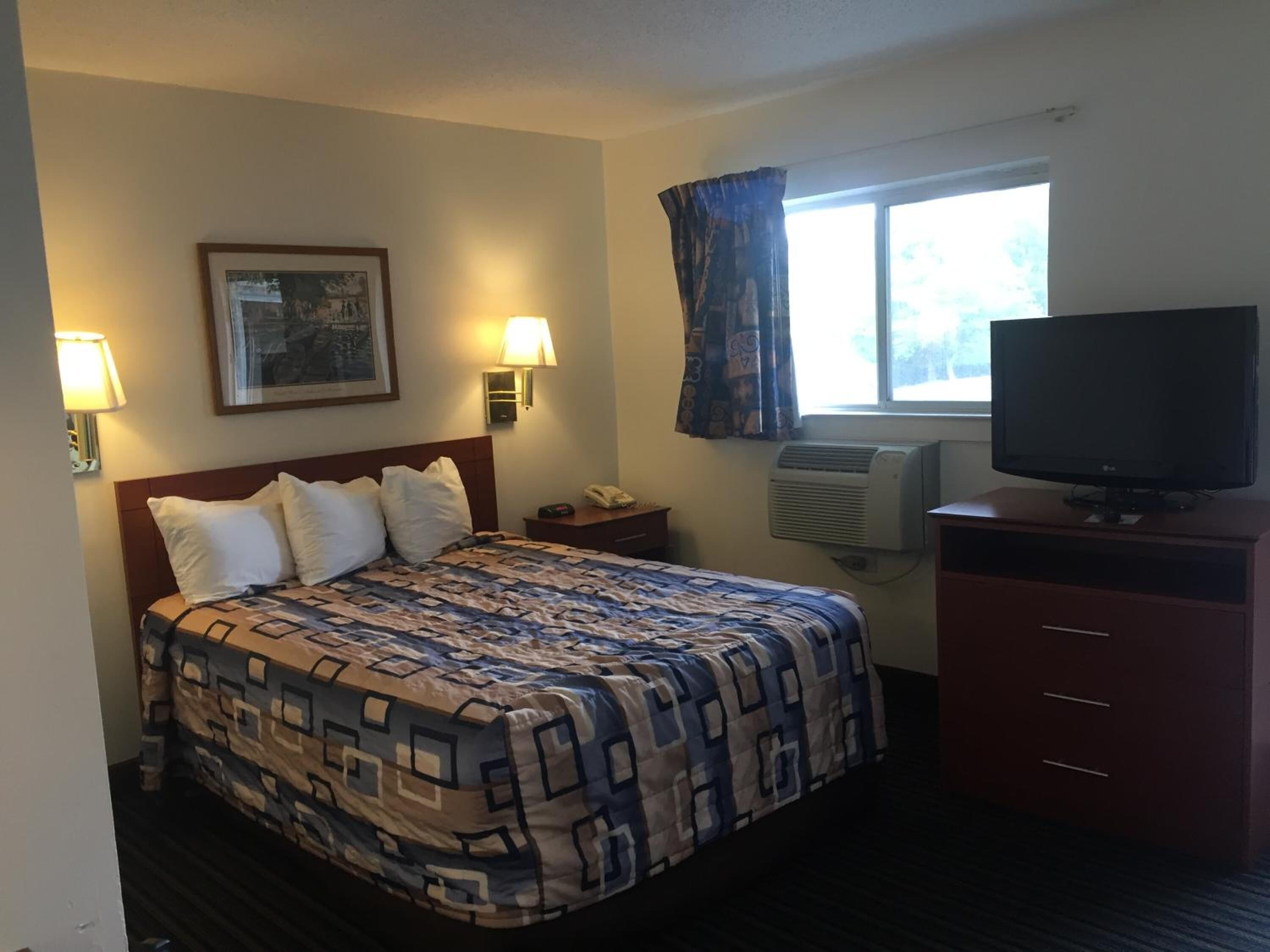 A hotel room with a bed, a TV, a desk, and a window.