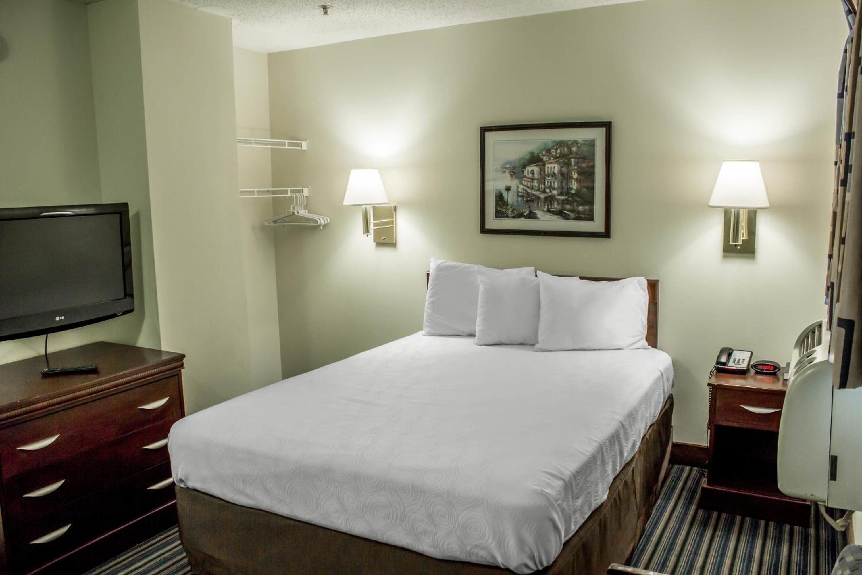 Une chambre d’hôtel avec un lit, une télévision, un bureau avec une lampe et un tableau au mur.