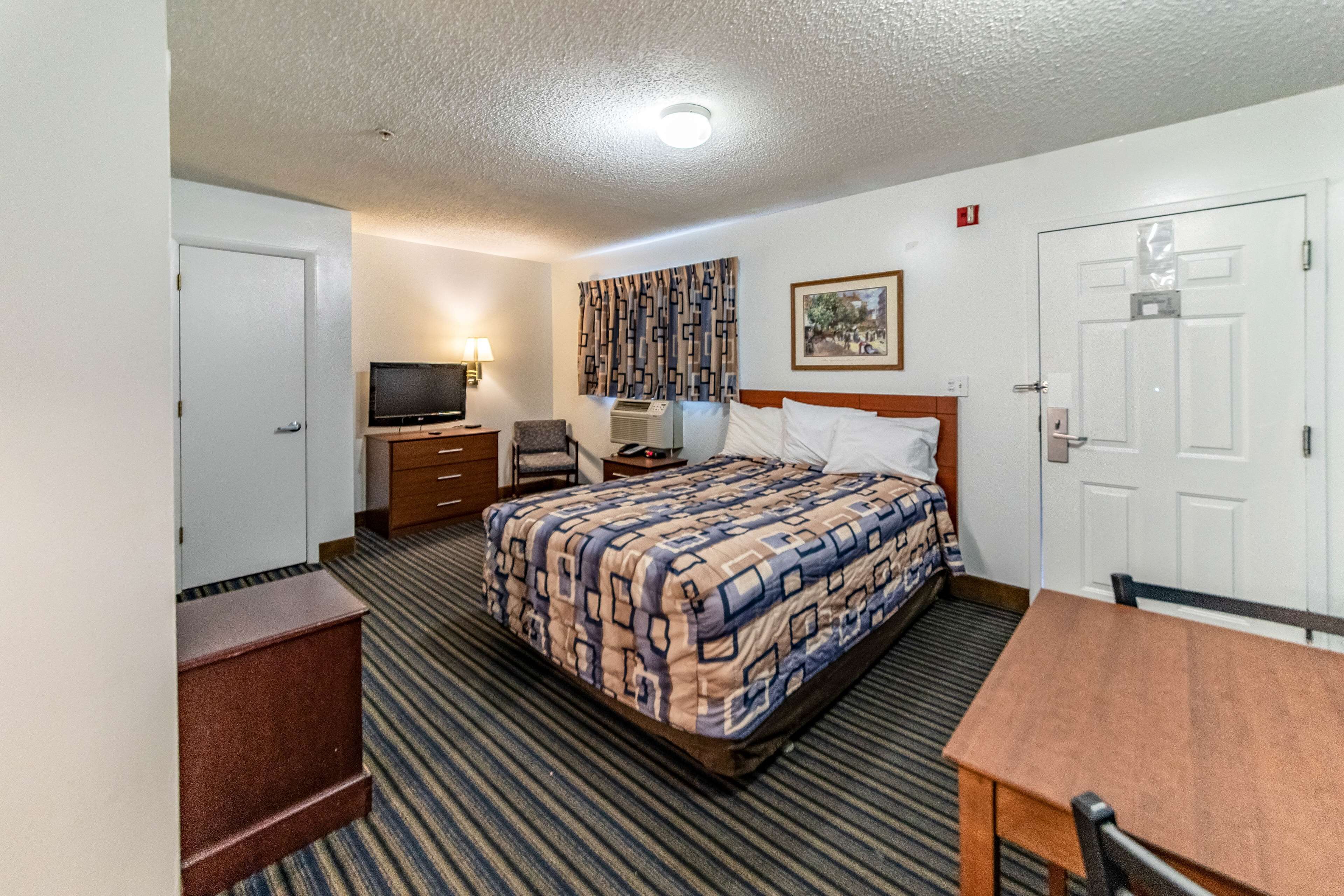 A hotel room with a bed, a desk, a chair, a television, and a wall-mounted air conditioner.