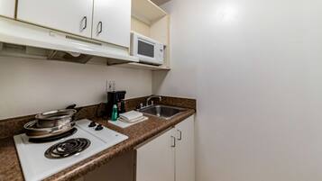 A compact kitchen with a microwave, stove, sink, and white cabinets.