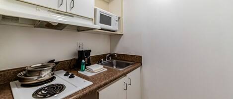 A compact kitchen with a microwave, stove, sink, and white cabinets.