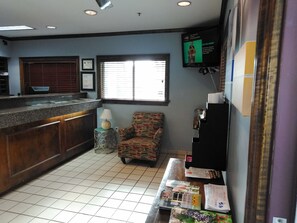 A reception area with a counter, a patterned armchair, a television mounted on the wall, and a window with blinds.