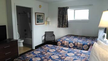 A bedroom with two beds, a chair, a desk, a window with curtains, a wall clock, and a framed picture.