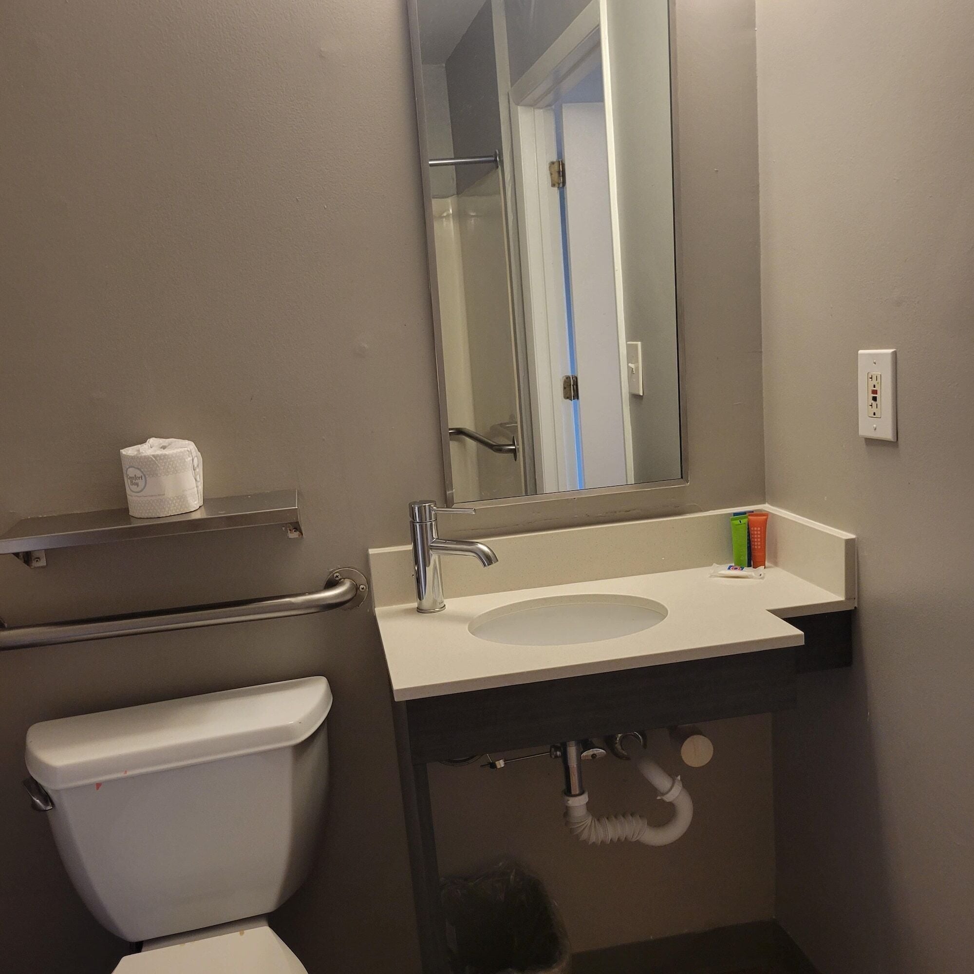A bathroom with a white toilet, a sink with a mirror above it, and a towel dispenser on the wall.