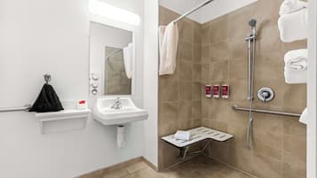 A modern bathroom with a sink, mirror, towel rack, shower, and handrails.