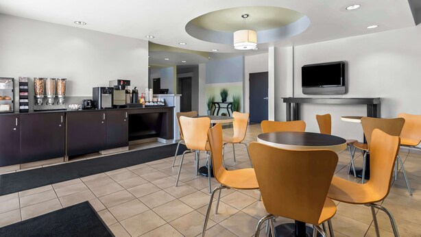 A modern dining area with a central round table, orange chairs, a kitchen counter with appliances, and a flat-screen TV mounted on the wall. - SureStay by Best Western Livingston Merced County (Livingston)