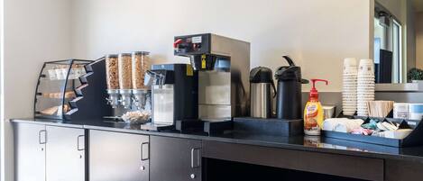 A coffee station with a coffee machine, condiment dispensers, and a variety of coffee pods.