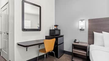 Habitació d'hotel senzilla amb cuina compacta, escriptori amb cadira, llit i una petita taula de nit amb telèfon.