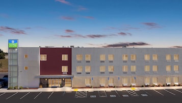 A modern hotel building with a red and grey facade, a parking lot with marked handicapped spaces, and a SureStay sign.