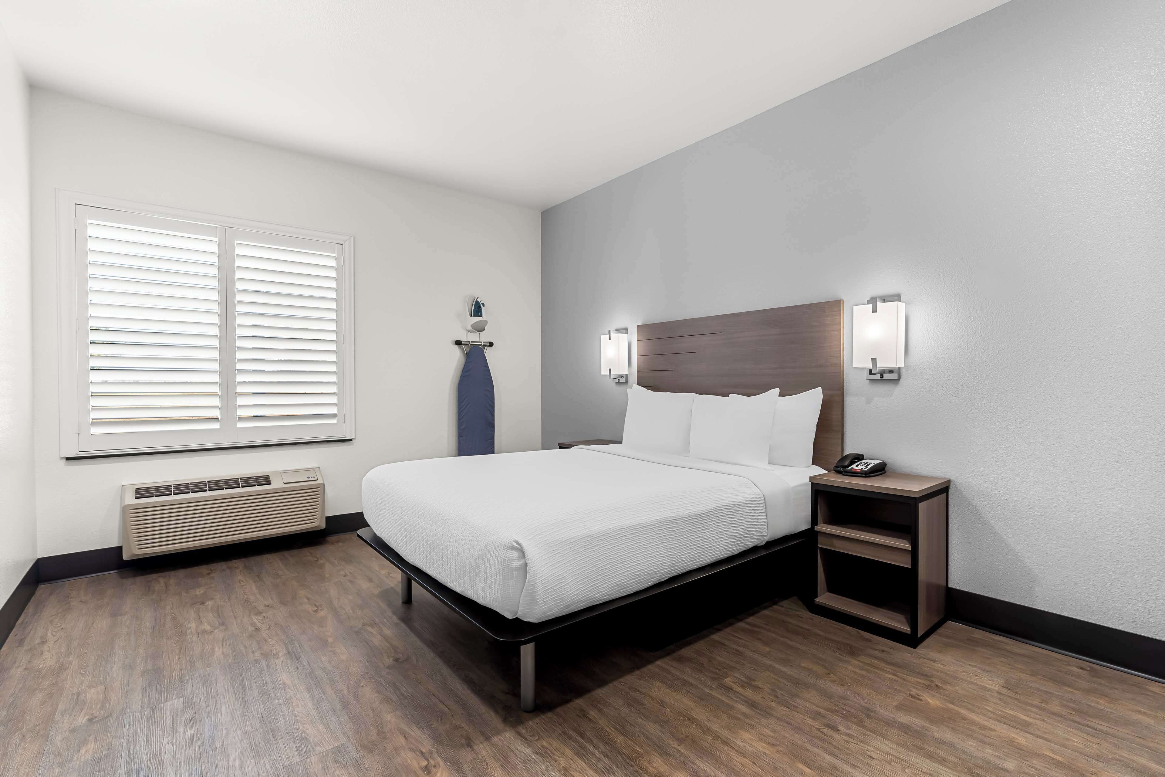 Une chambre d’hôtel moderne, dotée d’un grand lit, de tables de chevet, d’un radiateur fixé au mur et d’une fenêtre avec stores.