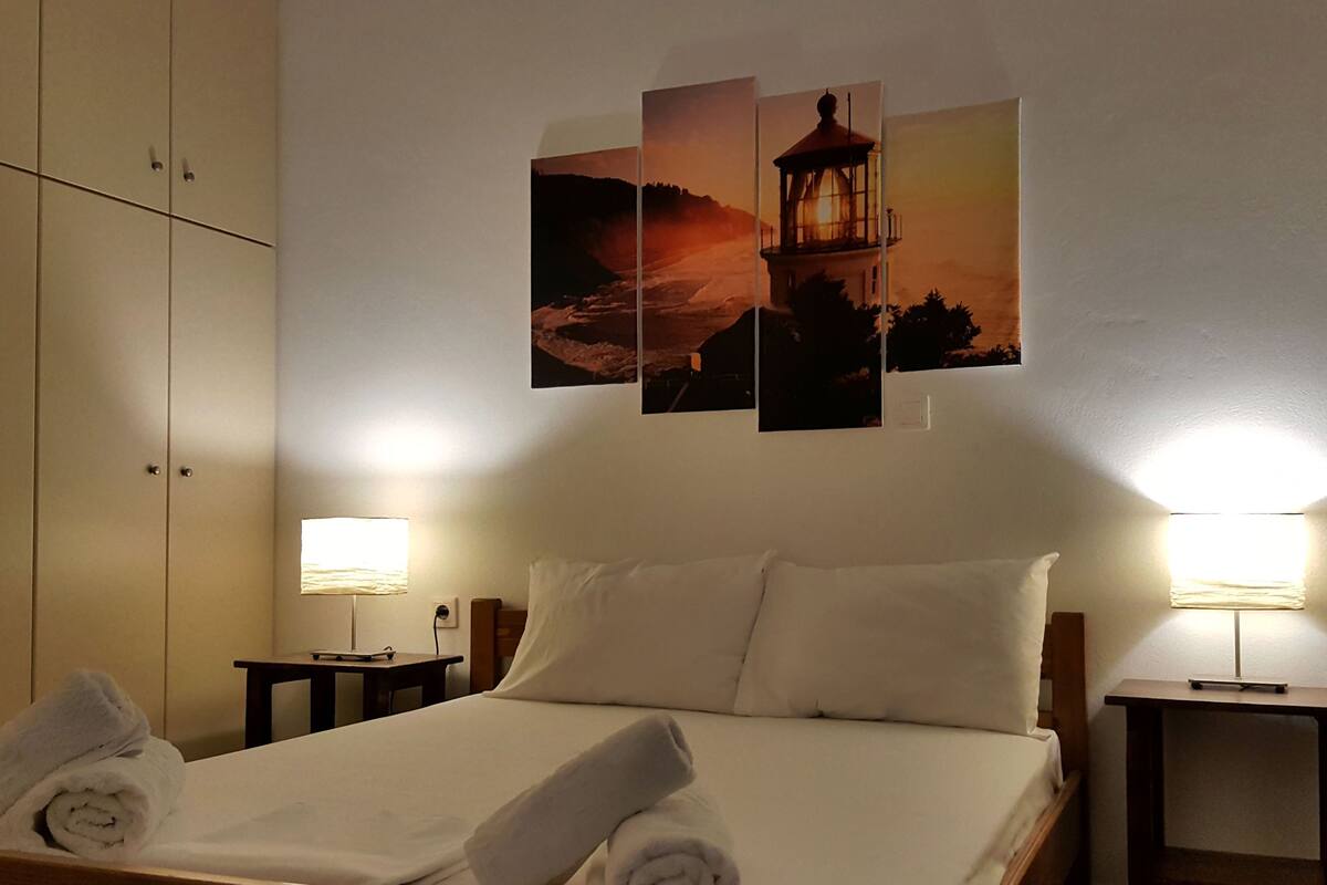 Ett hotellrum med en säng, två sänglampor, ett konstverk på väggen som föreställer en fyr och en garderob.