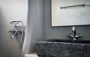 A bathroom with a stone sink, a handheld showerhead, and a wall-mounted towel rack. - Avissalou Apartments (Tinos)