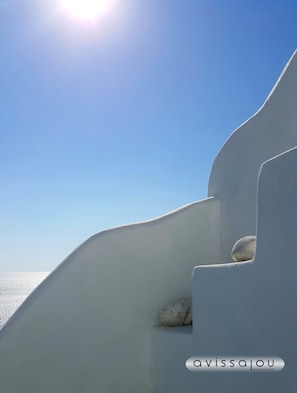 A white building with a curved facade and a stone element. - Avissalou Apartments (Tinos)