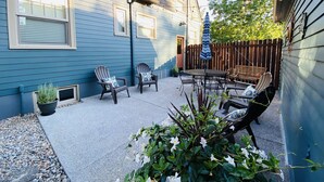 Una casa azul con un patio que tiene dos sillas Adirondack, una mesa y un paraguas colgante.