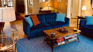 Una sala de estar con un sofá azul, una mesa de centro con juegos de mesa y una lámpara.