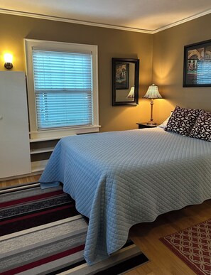 A bedroom with a bed, a nightstand, a lamp, a window with blinds, a framed picture, and a rug. - Peaceful Oasis Long-Term Stays 30+ Days Only Alberta Arts  Super Clean & Cozy  (Portland)