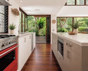 A modern kitchen with a central island, stainless steel appliances, and a view of a lush garden.
