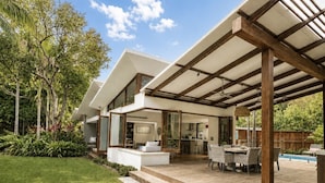 Ein modernes Haus mit überdachter Terrasse, Schwimmbecken und gepflegtem Rasen.
