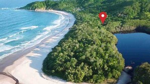 Luftaufnahme einer Küstenregion mit Strand, dichter Vegetation und einem roten Positionsmarker.