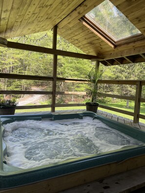 Un jacuzzi bajo una terraza de madera con vistas a un área boscosa.