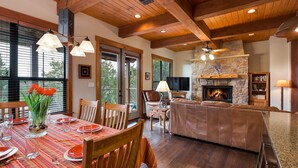 A spacious living area with a stone fireplace, wooden ceiling beams, and a dining area with a red tablecloth. - Scenic Luxury Home - Hollows Resort & Marina, Lake Travis, 4 Pools (Jonestown)
