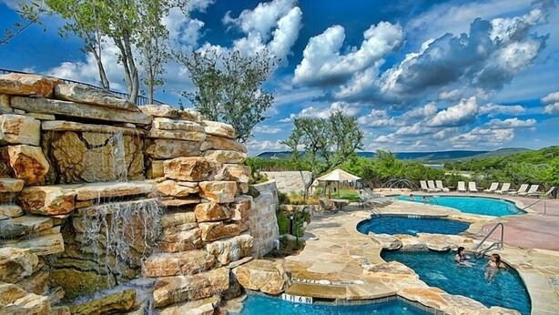 A pool area with multiple pools, a waterfall feature, and lounge chairs. - Scenic Luxury Home - Hollows Resort & Marina, Lake Travis, 4 Pools (Jonestown)