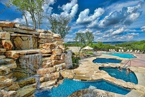 Un espace piscine comprenant plusieurs piscines, une cascade et des chaises longues.
