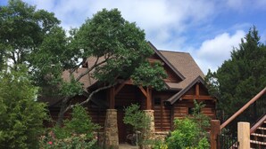 A log cabin with a stone foundation, wooden beams, and a covered porch. - Scenic Luxury Home - Hollows Resort & Marina, Lake Travis, 4 Pools (Jonestown)