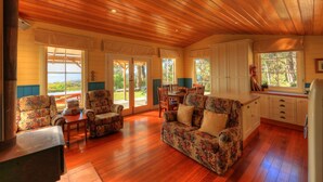 A cozy cabin interior with wooden floors, floral-patterned furniture, and large windows offering views of the outdoors. - Island View Spa Cottage (Smithton)