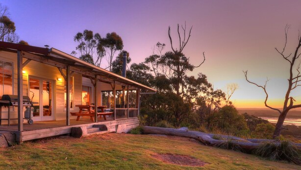A wooden house with a covered porch, picnic tables, and a barbecue grill. - Island View Spa Cottage (Smithton)