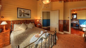 A bedroom with a bed, bedside lamps, a framed picture on the wall, and a bathroom visible through an open door. - Island View Spa Cottage (Smithton)