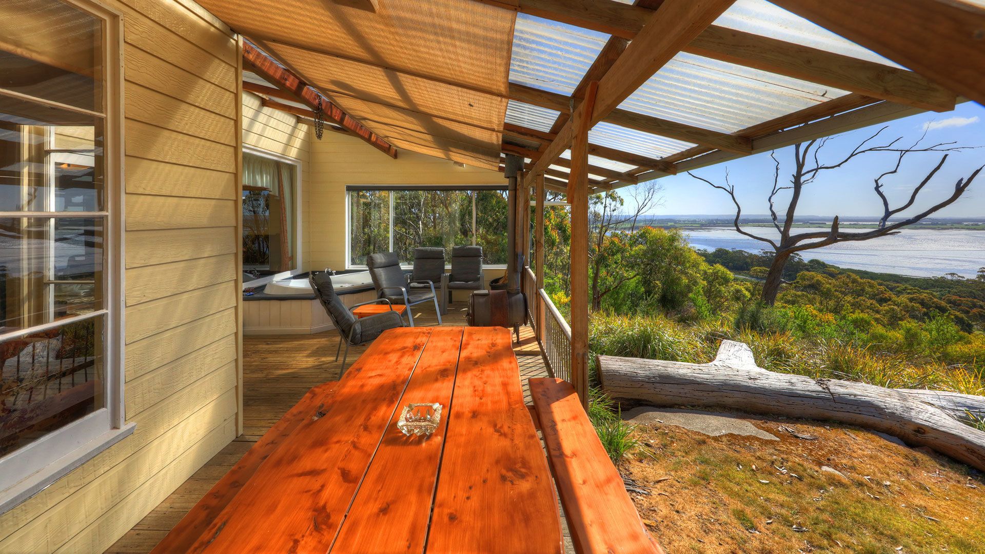 A wooden deck with a table and chairs, overlooking a scenic view of the ocean and hills.