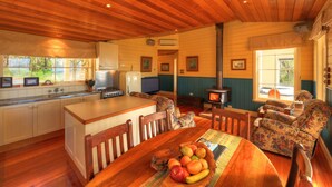 A cozy cabin interior with a kitchen, dining area, and a wood-burning stove. - Island View Spa Cottage (Smithton)