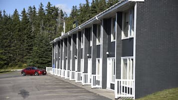Fileira de quartos de motel com corrimãos brancos e um carro vermelho estacionado em frente.