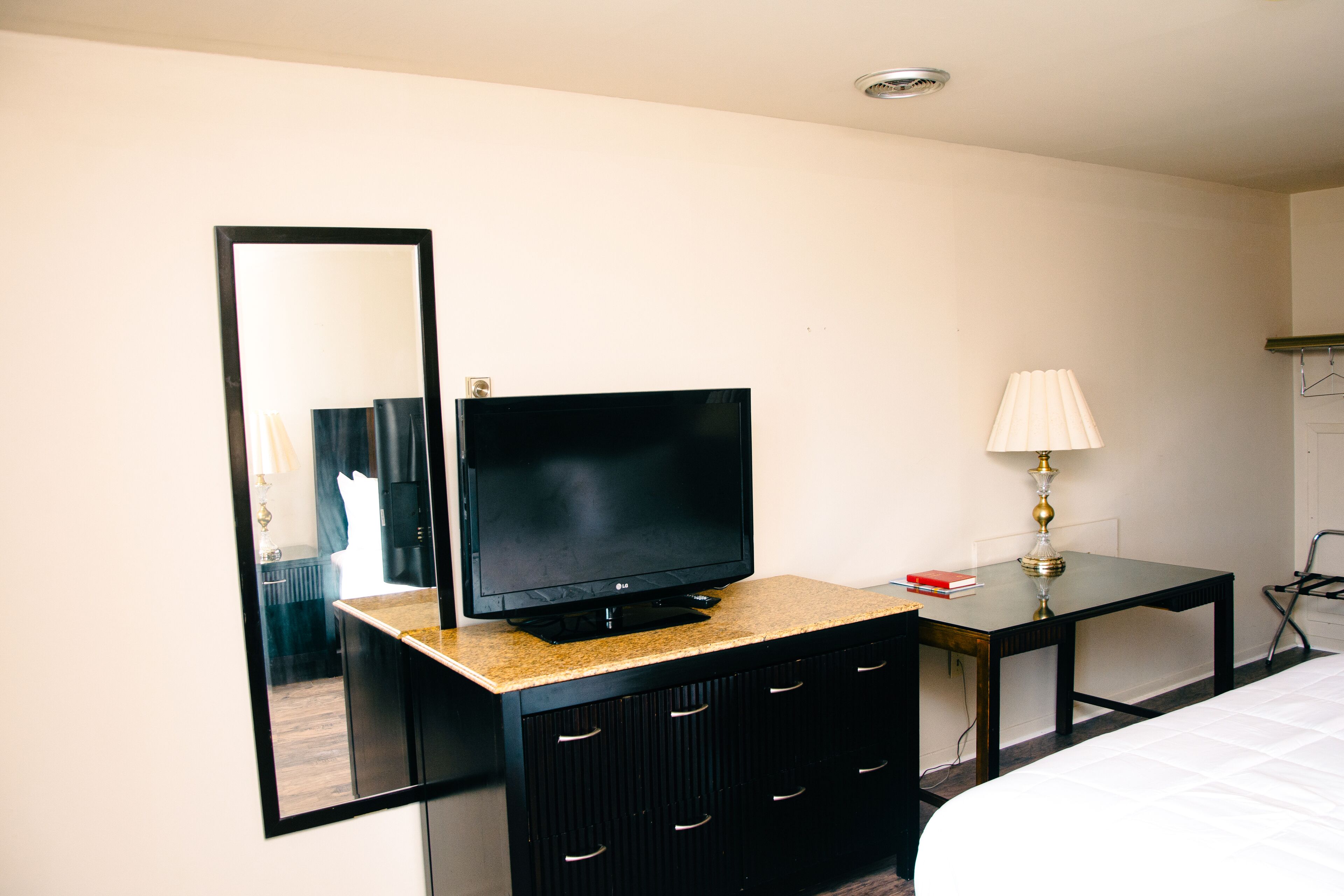 Una habitación de hotel con televisor en una cómoda, un espejo, una lámpara y una cama.